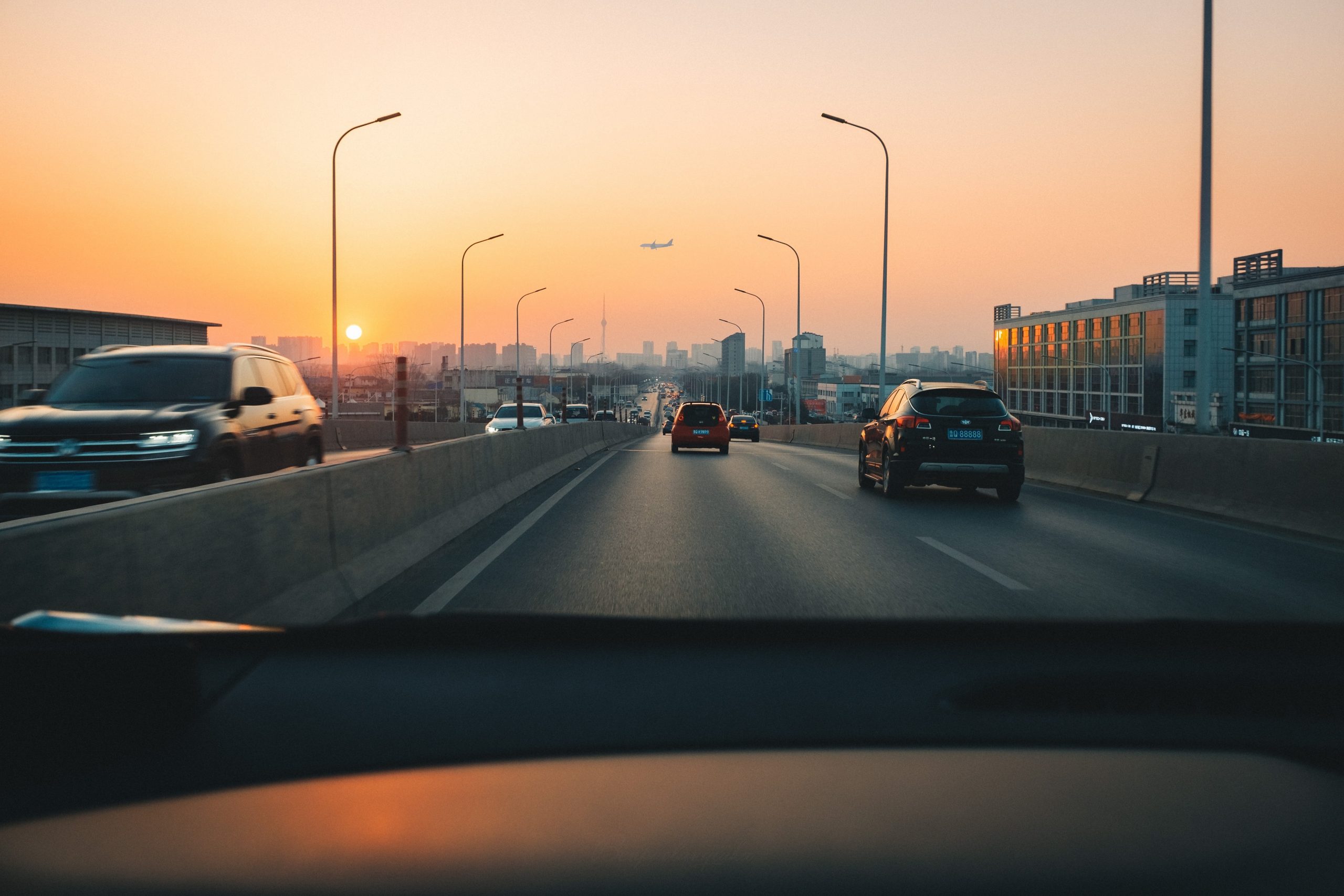 Cars driving on a highway with smog and sunset in the background of a cityscape